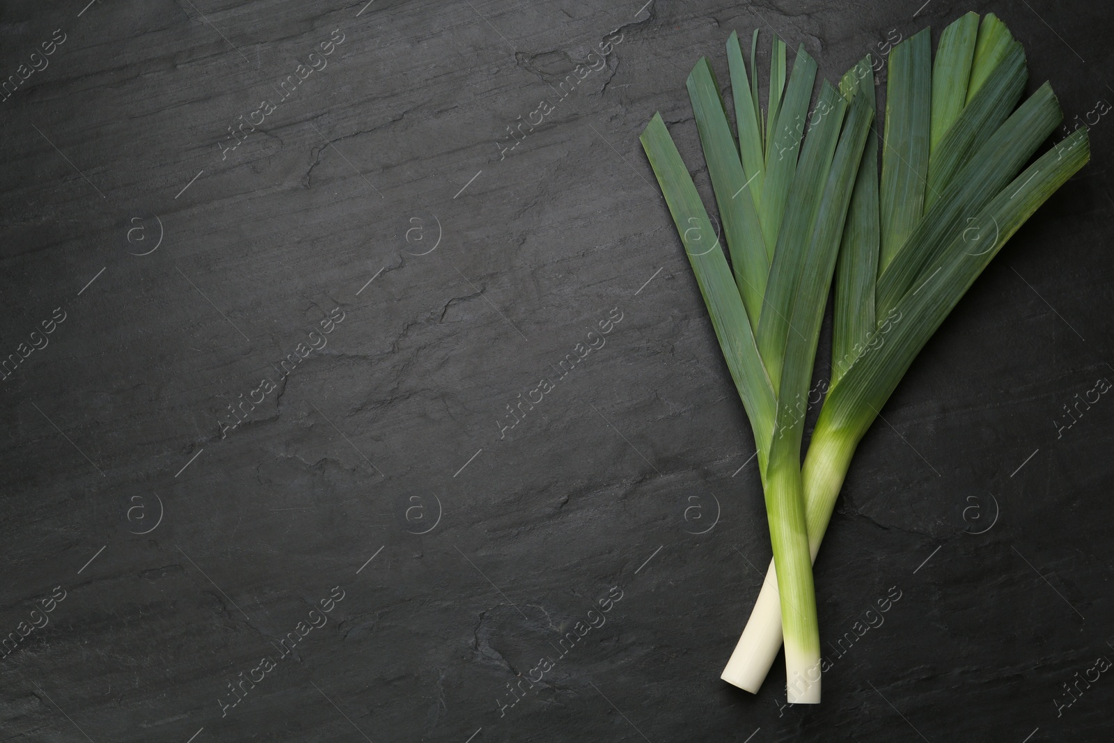 Photo of Fresh raw leeks on black table, flat lay. Space for text