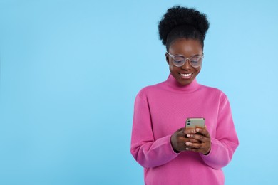 Photo of Happy young woman with smartphone on light blue background. Space for text