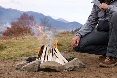 Photo of Man near bonfire in mountains, closeup. Camping season
