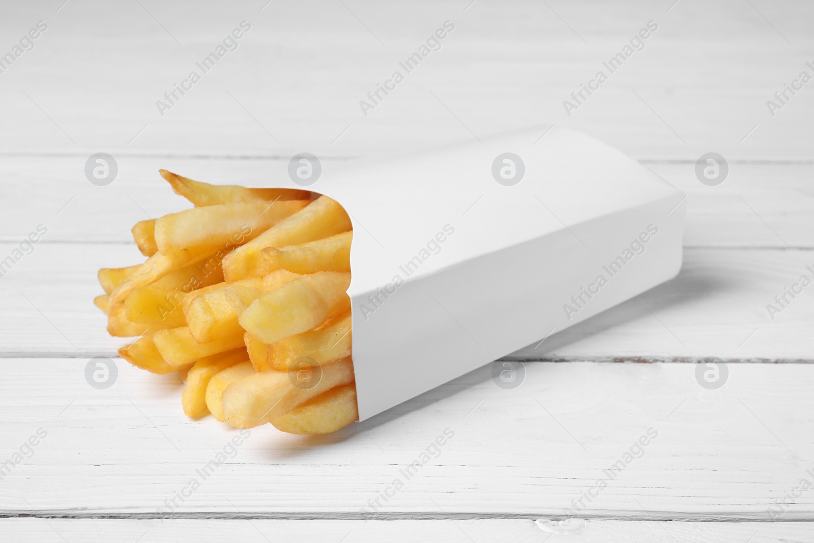 Photo of Delicious french fries in paper box on white wooden table, closeup