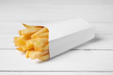 Photo of Delicious french fries in paper box on white wooden table, closeup