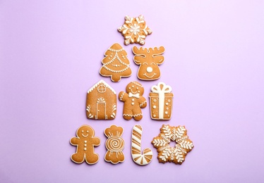 Christmas tree shape made of delicious decorated gingerbread cookies on lilac background, flat lay
