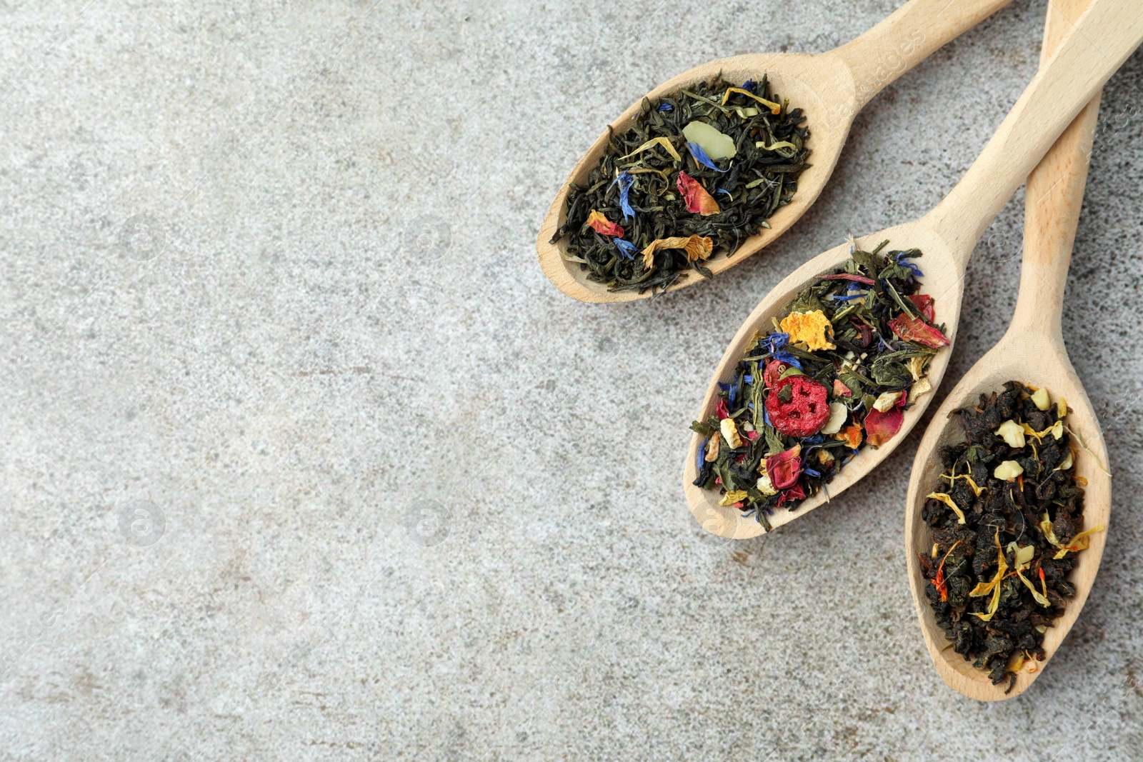 Photo of Different kinds of dry herbal tea in wooden spoons on light grey table, flat lay. Space for text