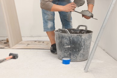 Worker applying adhesive mix on spatula near tile indoors, closeup