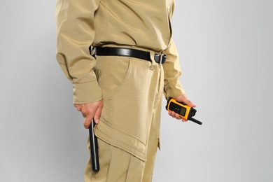Photo of Male security guard in uniform with portable radio transmitter and police baton on grey background, closeup