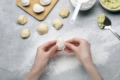 Woman making dumplings (varenyky) with potato at grey table, top view