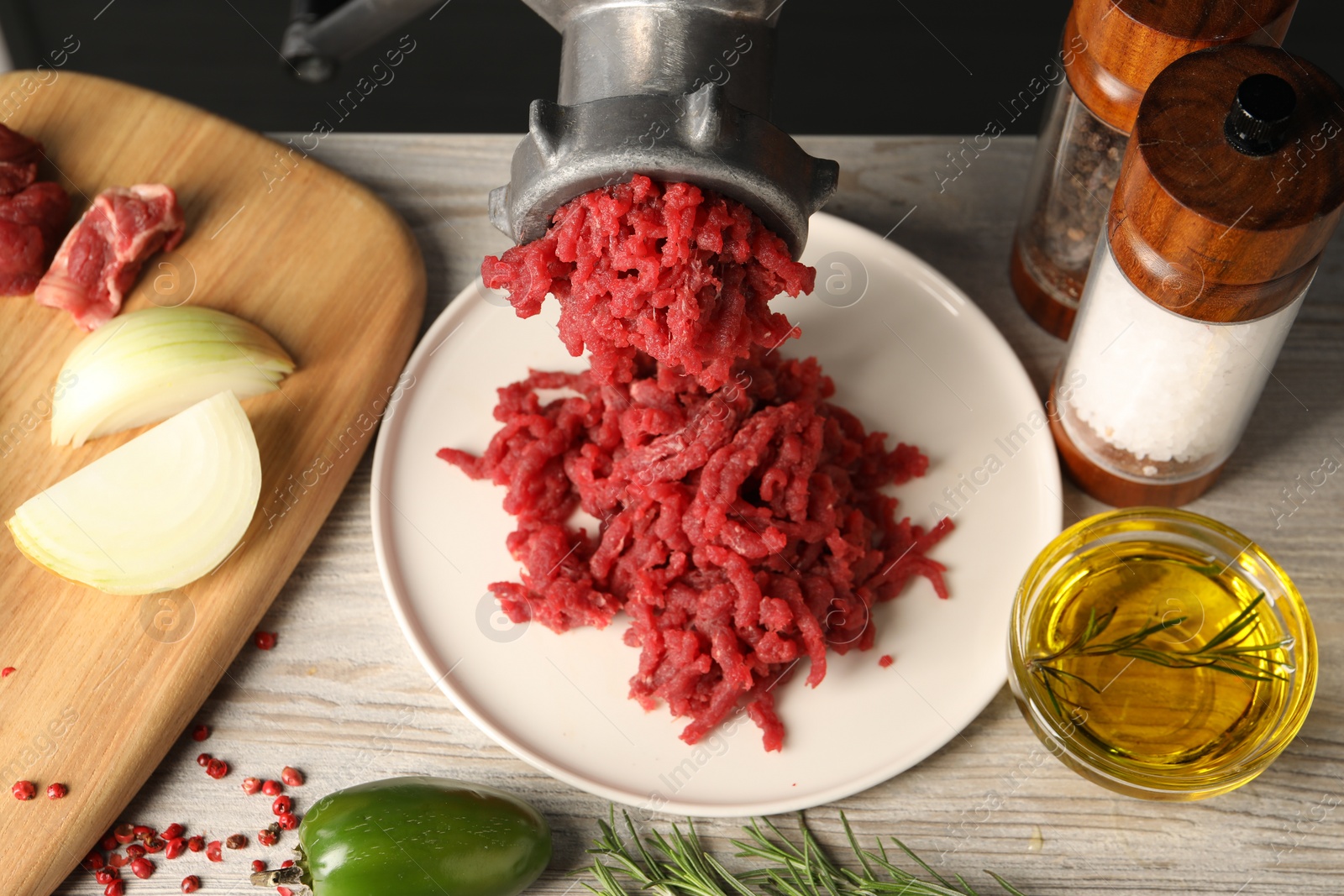 Photo of Metal meat grinder with minced beef and spices on light wooden table
