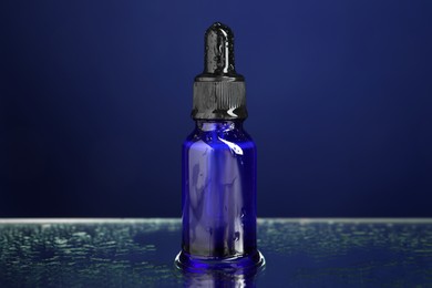 Photo of Bottle of face serum on wet surface against blue background, closeup