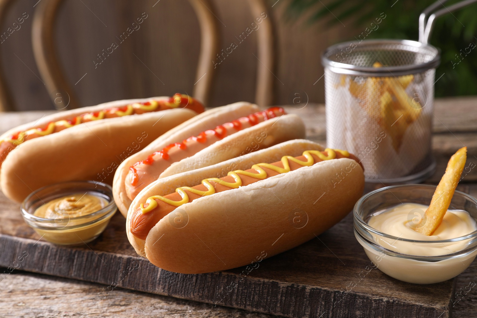 Photo of Delicious hot dogs with sauces and French fry on wooden table, closeup