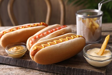 Photo of Delicious hot dogs with sauces and French fry on wooden table, closeup