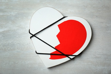 Half of cut paper heart tied with cord to detail on gray background, top view. Relationship problems