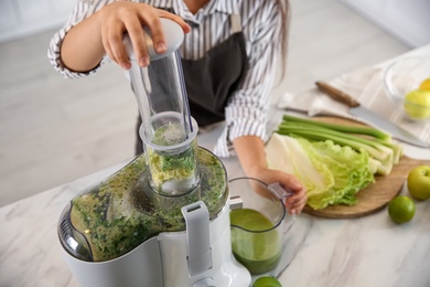 Photo of Young woman making tasty fresh juice at table in kitchen, closeup