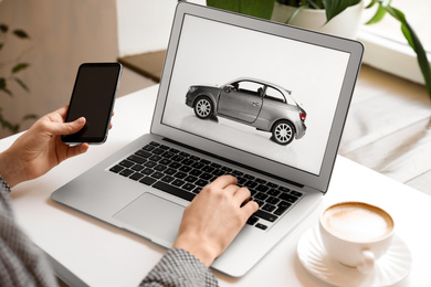 Photo of Woman using laptop and phone to buy car at table indoors, closeup