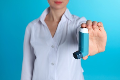 Female doctor holding asthma inhaler on color background, closeup. Medical object