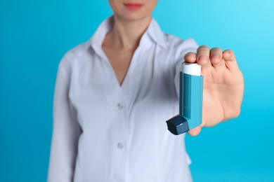 Photo of Female doctor holding asthma inhaler on color background, closeup. Medical object