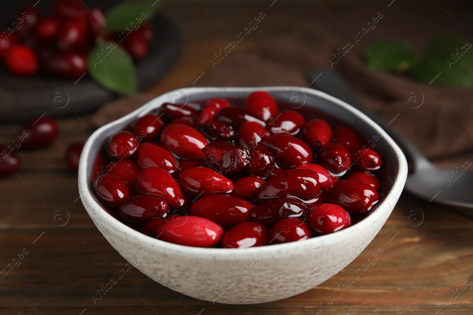 Photo of Delicious dogwood jam with berries in bowl on wooden table, closeup