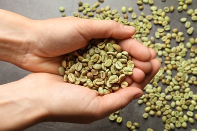 Woman holding pile of green coffee beans over grey table, closeup
