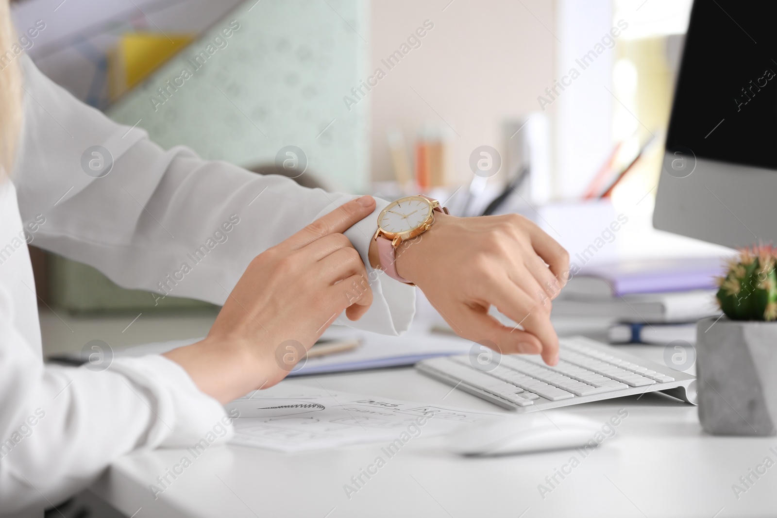 Photo of Young woman checking time on her wristwatch at workplace