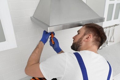 Photo of Worker repairing modern cooker hood in kitchen