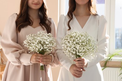 Bride and her bridesmaid with beautiful bouquet indoors, closeup. Wedding day