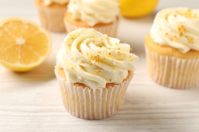 Photo of Tasty cupcakes with cream, zest and lemons on white wooden table, closeup