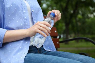 Photo of Woman with bottle of water sitting on bench outdoors, closeup