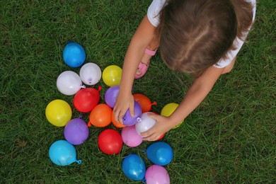 Little girl with water bombs on green grass, top view