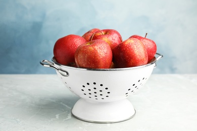 Colander with ripe juicy red apples on grey table against blue background