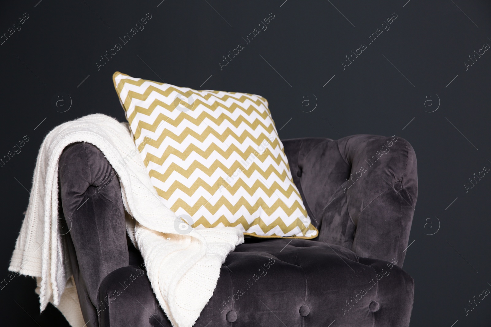 Photo of Stylish armchair with pillow and plaid near dark wall. Idea for interior design