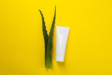 Aloe vera toothpaste in blank tube and green leaves on yellow background, flat lay. Space for text