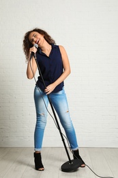 Photo of Curly African-American woman singing in microphone near brick wall