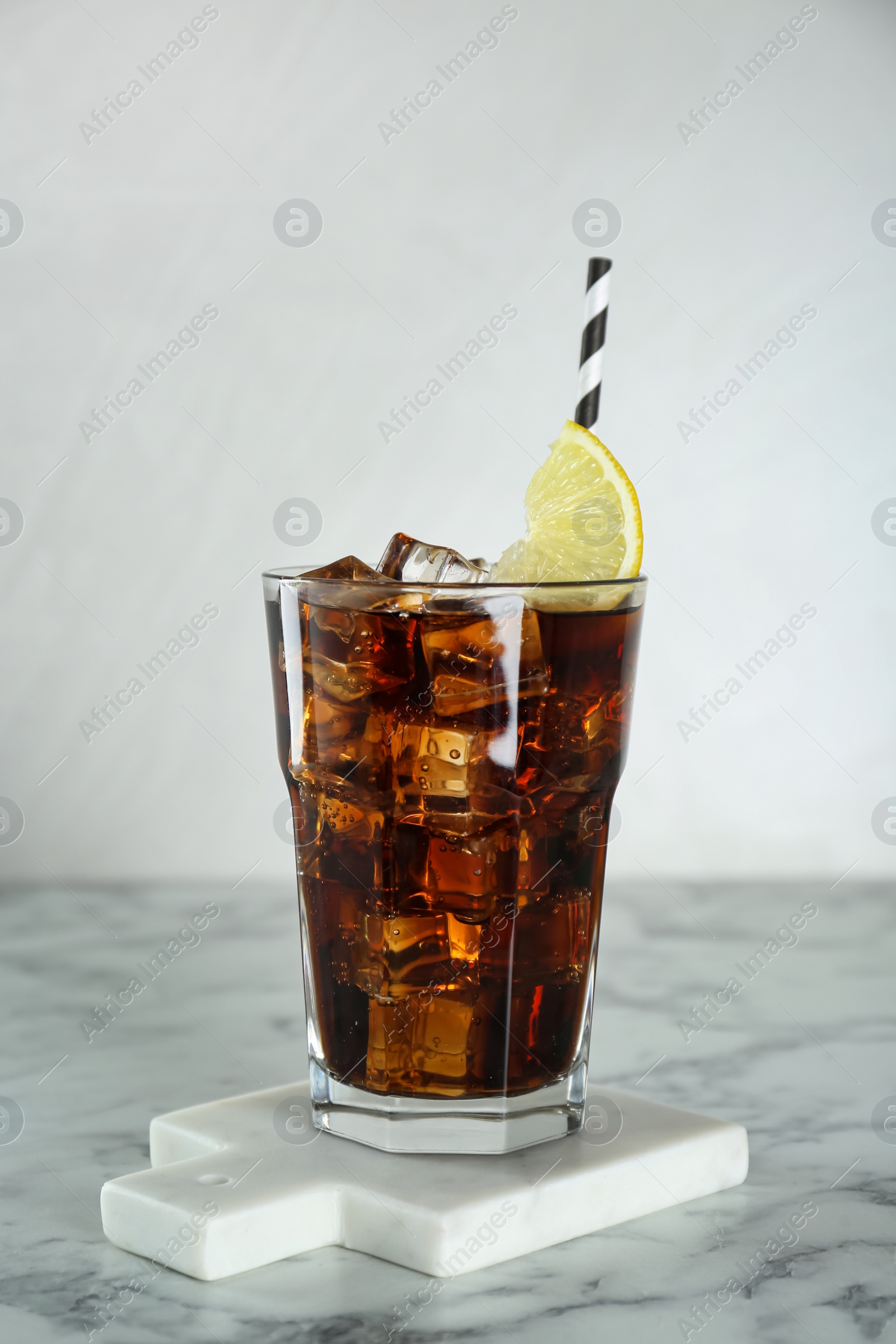 Photo of Glass of refreshing soda water with ice cubes and lemon slice on white marble table