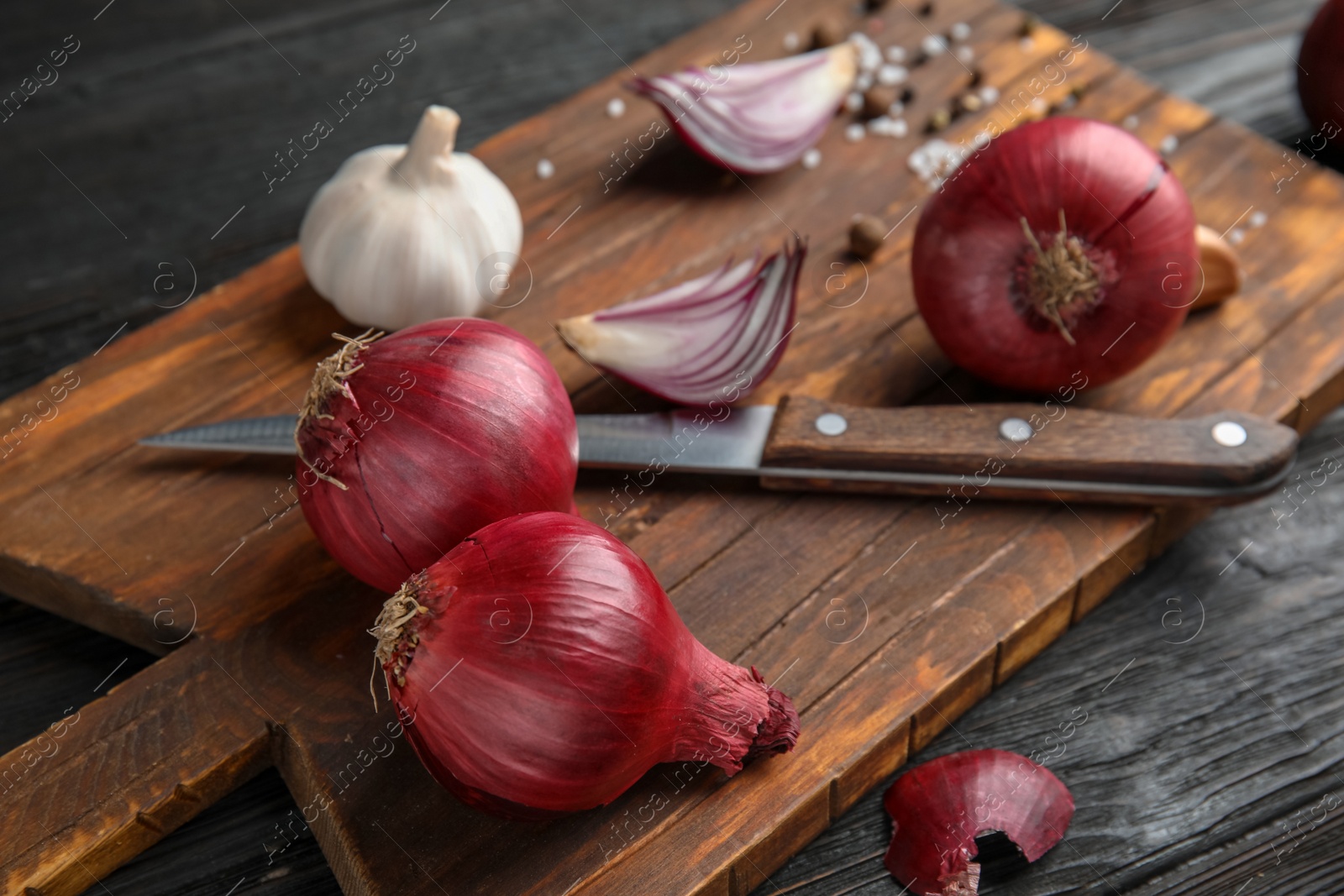 Photo of Wooden board with ripe red onions on table, closeup