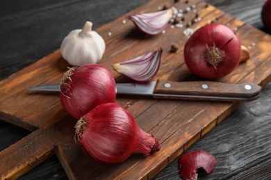 Wooden board with ripe red onions on table, closeup