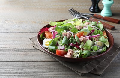 Photo of Bowl of delicious salad with canned tuna and vegetables on wooden table, space for text