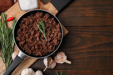Photo of Fried ground meat in frying pan and products on wooden table, flat lay. Space for text