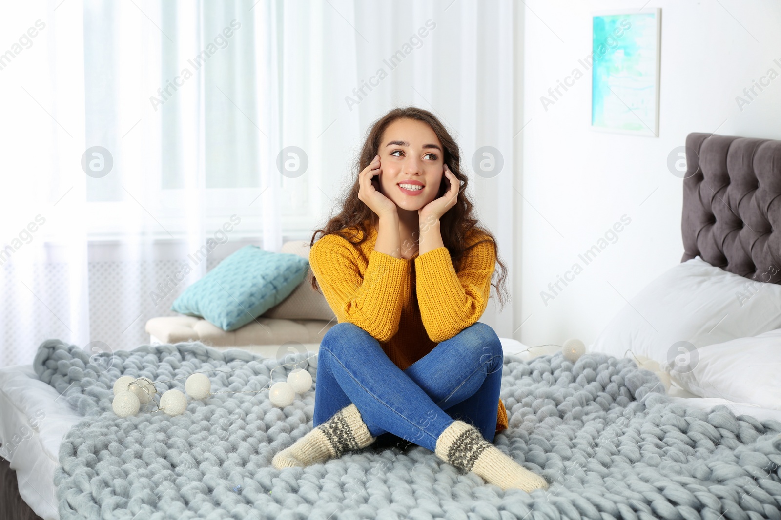 Photo of Young beautiful woman in warm sweater on bed at home