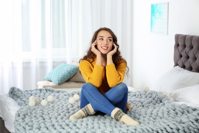 Photo of Young beautiful woman in warm sweater on bed at home