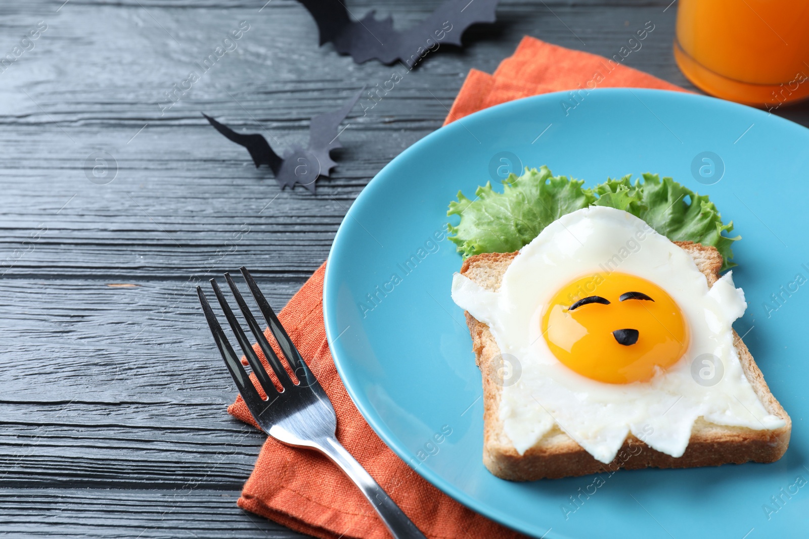 Photo of Halloween themed breakfast served on black wooden table, closeup. Tasty toast with fried egg in shape of ghost