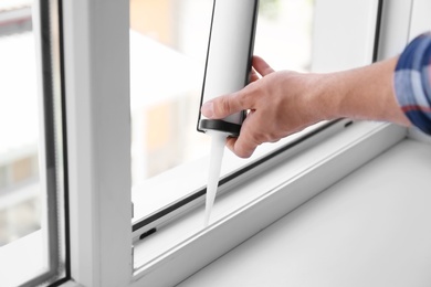 Photo of Construction worker sealing window with caulk indoors