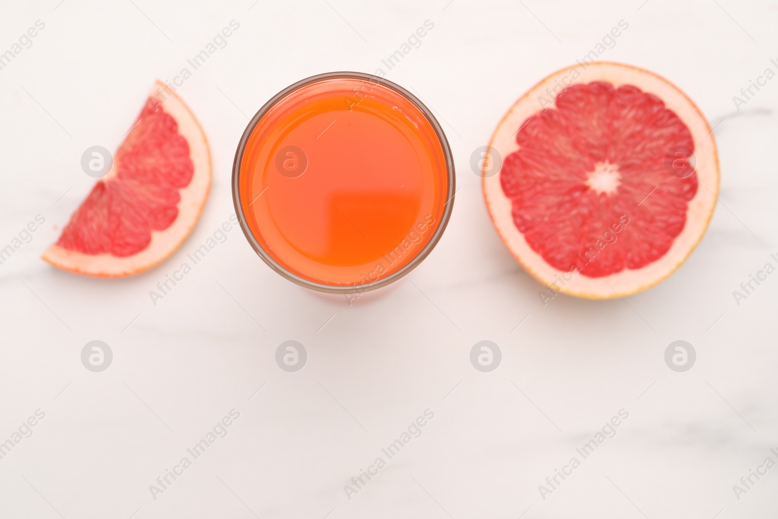 Photo of Tasty grapefruit juice in glass and slices of fresh fruit on white table, top view. Space for text