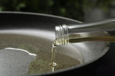 Pouring cooking oil from bottle into frying pan, closeup