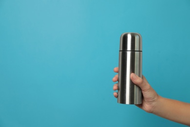 Photo of Woman holding modern thermos on light blue background, closeup. Space for text
