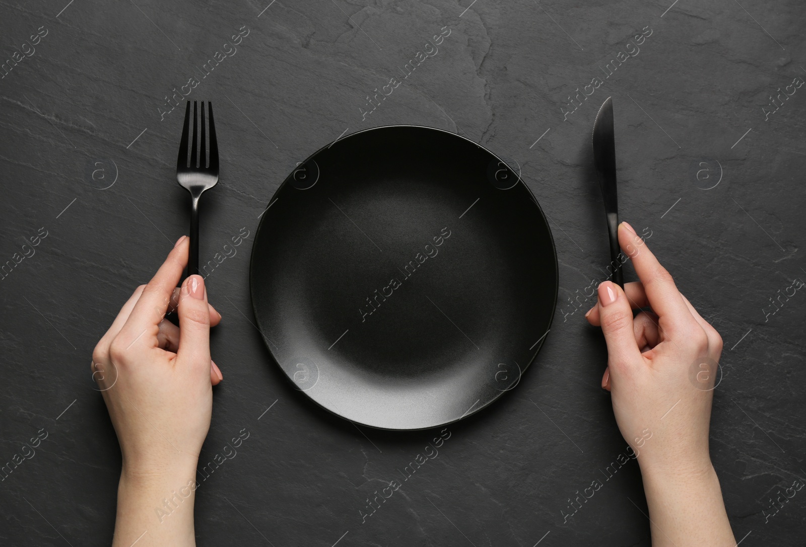 Photo of Woman with empty plate and cutlery at black table, top view