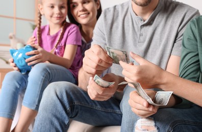 Photo of Happy family with money and piggy bank at home, closeup