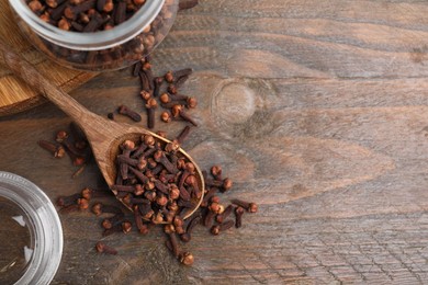 Photo of Glass jar and spoon with aromatic cloves on wooden table, flat lay. Space for text