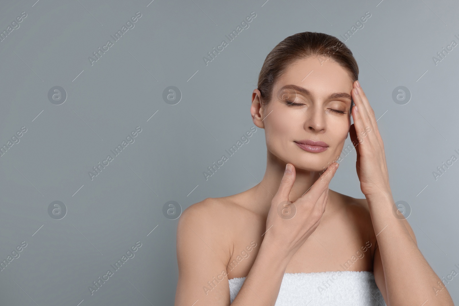 Photo of Woman massaging her face on grey background. Space for text