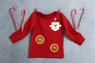 Photo of Red jumper and candy canes hanging on grey wall. Christmas baby clothes