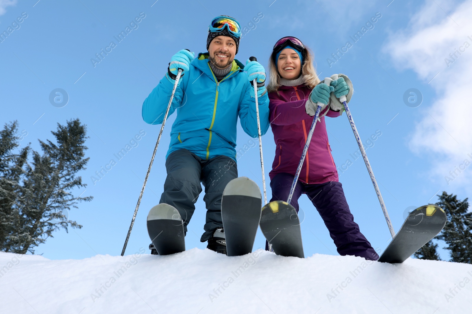 Photo of Happy couple with ski equipment outdoors, view from below. Winter vacation