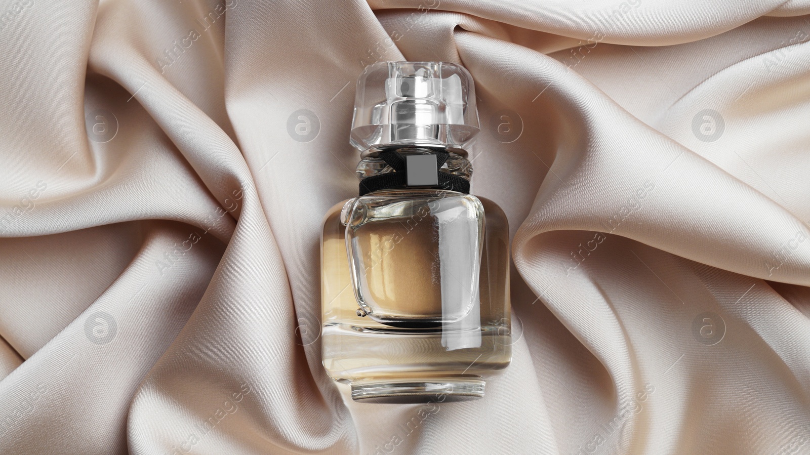 Photo of Luxury bottle of perfume on beige silk, top view